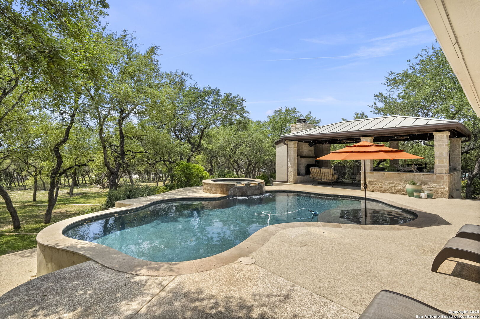 Located in the prestigious, gated community of Stone Creek Ranch, this exquisite Texas Hill Country home offers a rare combination of privacy, luxury, and thoughtful design.  From the moment you arrive, you're greeted by a circular drive framed by mature trees and Hill Country charm. Inside, a grand entryway with a dramatic curved staircase sets the tone for the spacious, open-concept living areas. The heart of the home is a chef's dream kitchen featuring a 6-burner gas stove, large center island with granite countertops, and a walk-in pantry. The primary suite is a sanctuary, complete with a spa-style bath featuring a walk-in shower, jetted tub, dual vanities, and generous closet space. A second bedroom suite downstairs is perfect for guests or multi-generational living. Upstairs, you'll find three additional bedrooms and a game room, offering ample room for entertainment and relaxation. Step outside to your private backyard retreat with a covered patio, outdoor kitchen, and heated in-ground pool and spa-all surrounded by lush landscaping and privacy trees on your 1+ acre lot.