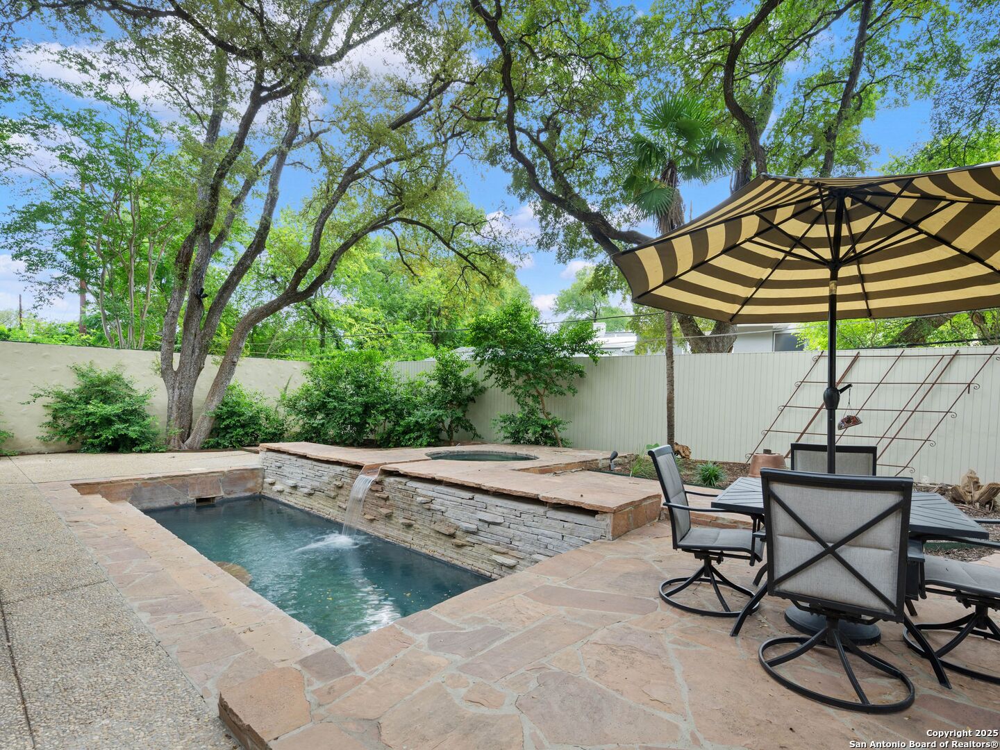 An architectural gem in the heart of San Antonio, this refined residence blends historic charm with the modern sophistication today's luxury buyers expect. The stately 3-bedroom, 2.5-bath main home has been meticulously reimagined with exceptional craftsmanship and is accompanied by two additional living quarters located at the rear of the property. Inside, vaulted ceilings, heirloom-quality finishes, and custom cabinetry create a timeless setting. The chef's kitchen is both striking and functional, featuring hand-selected stone, high-end fixtures, and seamless cabinetry designed for elevated everyday living. Just off the main living area, a sunroom framed by exposed wooden beams and artisan tile serves as a year-round retreat, ideal for quiet mornings or refined entertaining. The upstairs primary suite offers a private escape, with a sculptural soaking tub, expansive walk-in shower, and custom built-ins that balance luxury with thoughtful design. Outdoor living takes center stage with a deep covered veranda overlooking a professionally landscaped backyard. A cascading waterfall flows into a glistening pool, framed by mature foliage for complete privacy and tranquility. A fully detached two-story guest house completes the estate, featuring two private bedrooms, two full bathrooms, and a full kitchen. Perfect for hosting extended family, accommodating staff, or generating income, this separate residence offers rare flexibility without compromising the integrity of the main home. Situated in a quiet residential enclave just minutes from The Pearl and San Antonio's cultural corridor, this legacy property in Olmos Park offers timeless architecture, exceptional craftsmanship, and a lifestyle rooted in privacy and prestige.